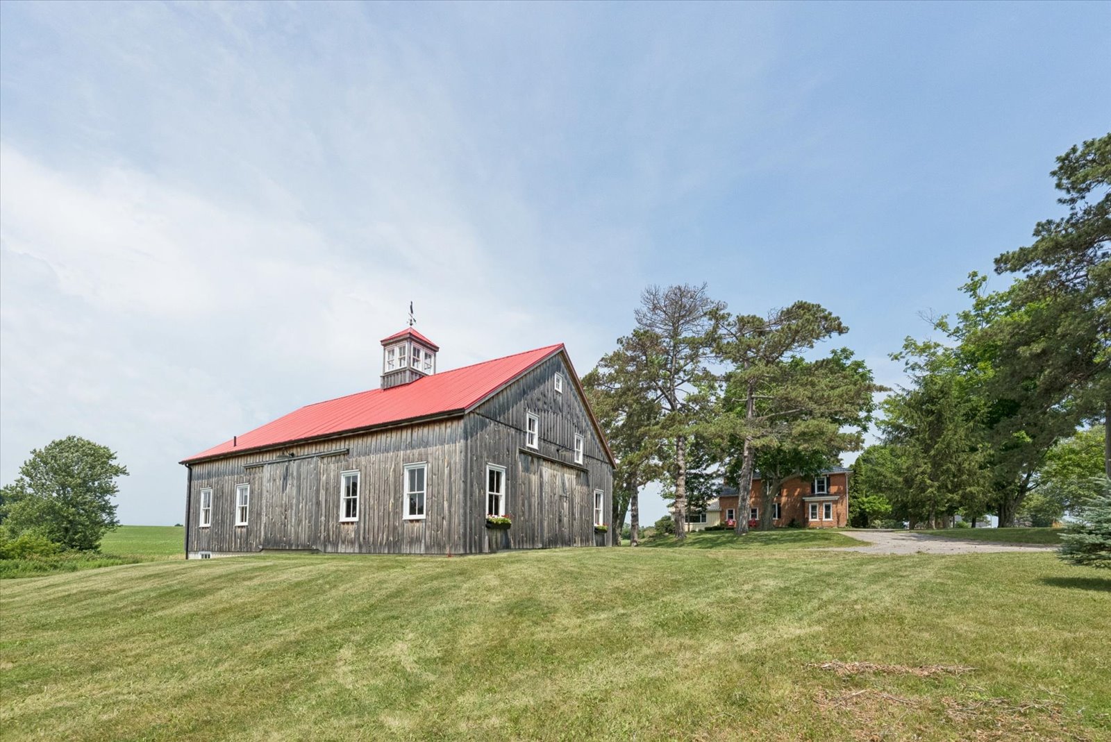 The barn's long weathered elevation with red roof and farmhouse beyond