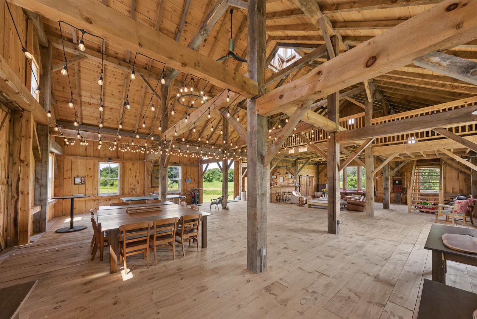 Timber-framed barn interior with string lights, dining table and loft
