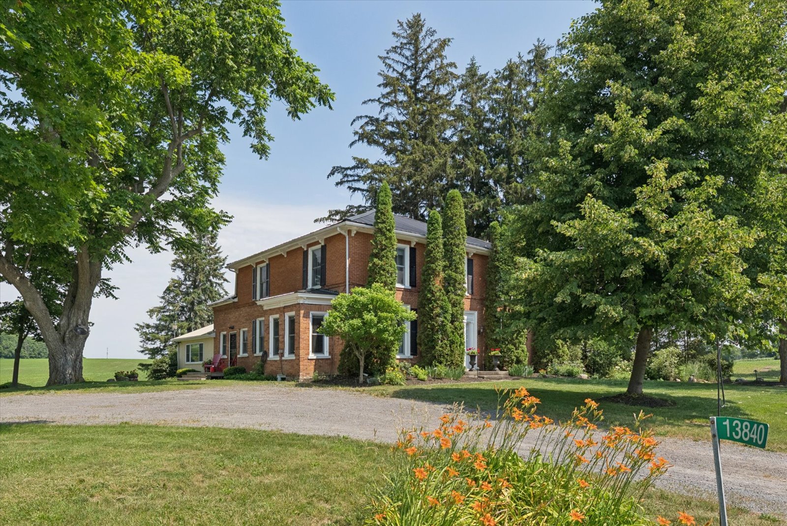 The 1847 brick farmhouse framed by mature trees and summer gardens